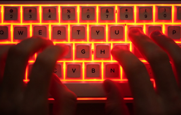 In this photo illustration, a young man types on an illuminated computer keyboard.